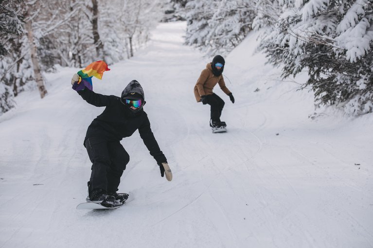 Snowboarders ridng with a rainbow flag