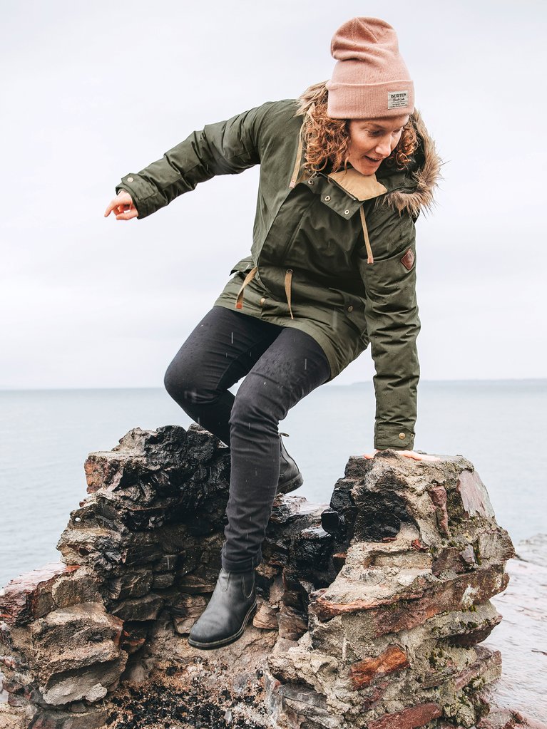 A woman wearing a Burton Saxton jacket and climbing on rocks in the rain.