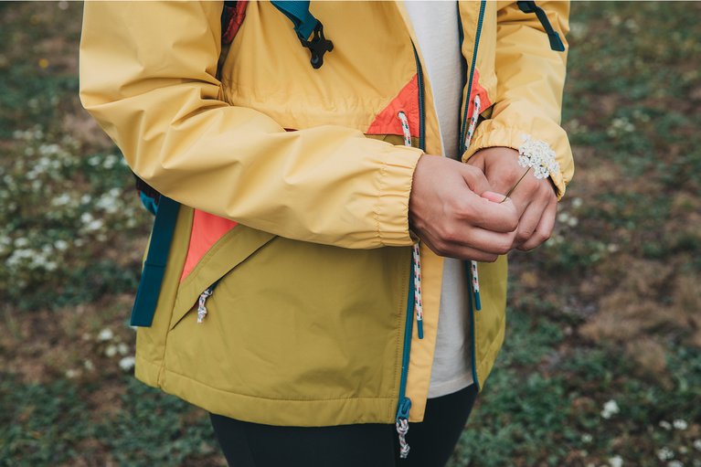 A rain shell-wearing adventurer holding a flower.