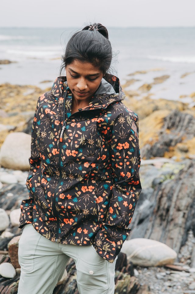 A woman walking on the beach in a rain jacket.
