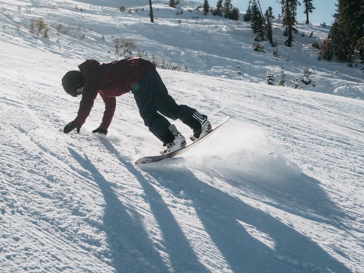 2) Während du dich herunterbeugst, damit deine Hände den Schnee erreichen, rutscht das Snowboard ganz von selbst von deinem Oberkörper weg. Lass deinen hinteren Fuß sich vom Boden lösen und dein Snowboard mit sich ziehen, sodass der Tail deines Boards zum Himmel zeigt.